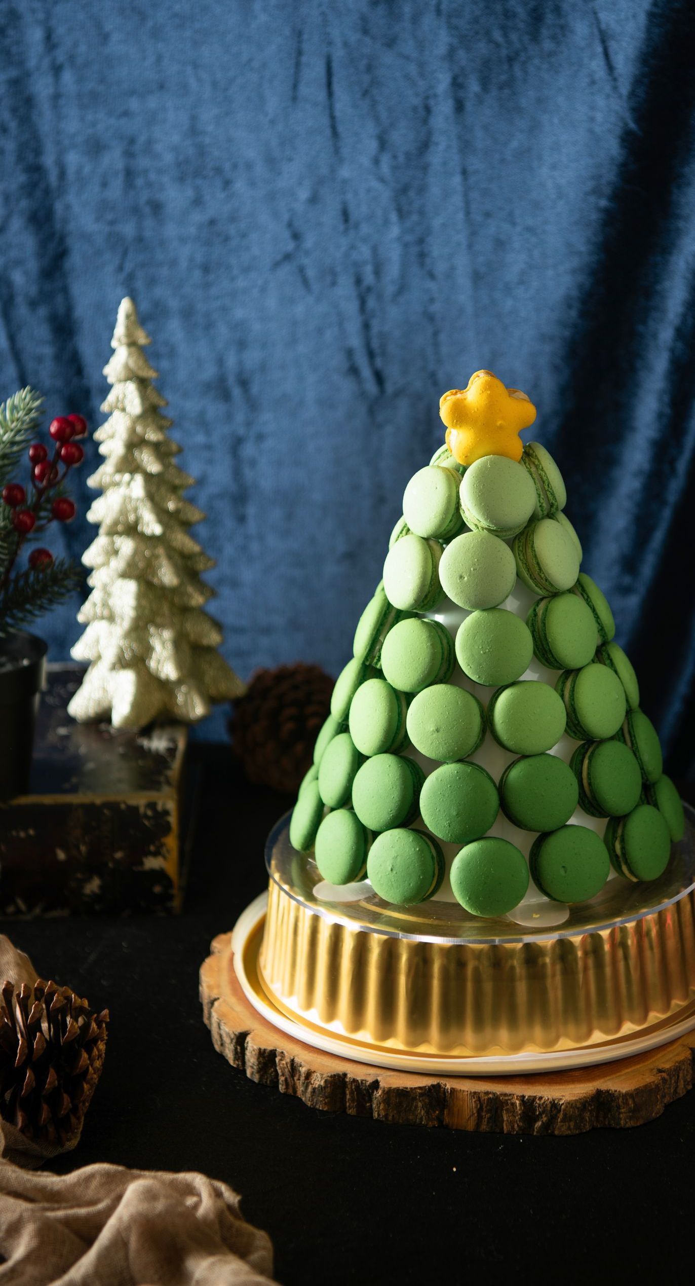 Green macaron Christmas tree on a gold base, with a yellow star on top, against a blue background.