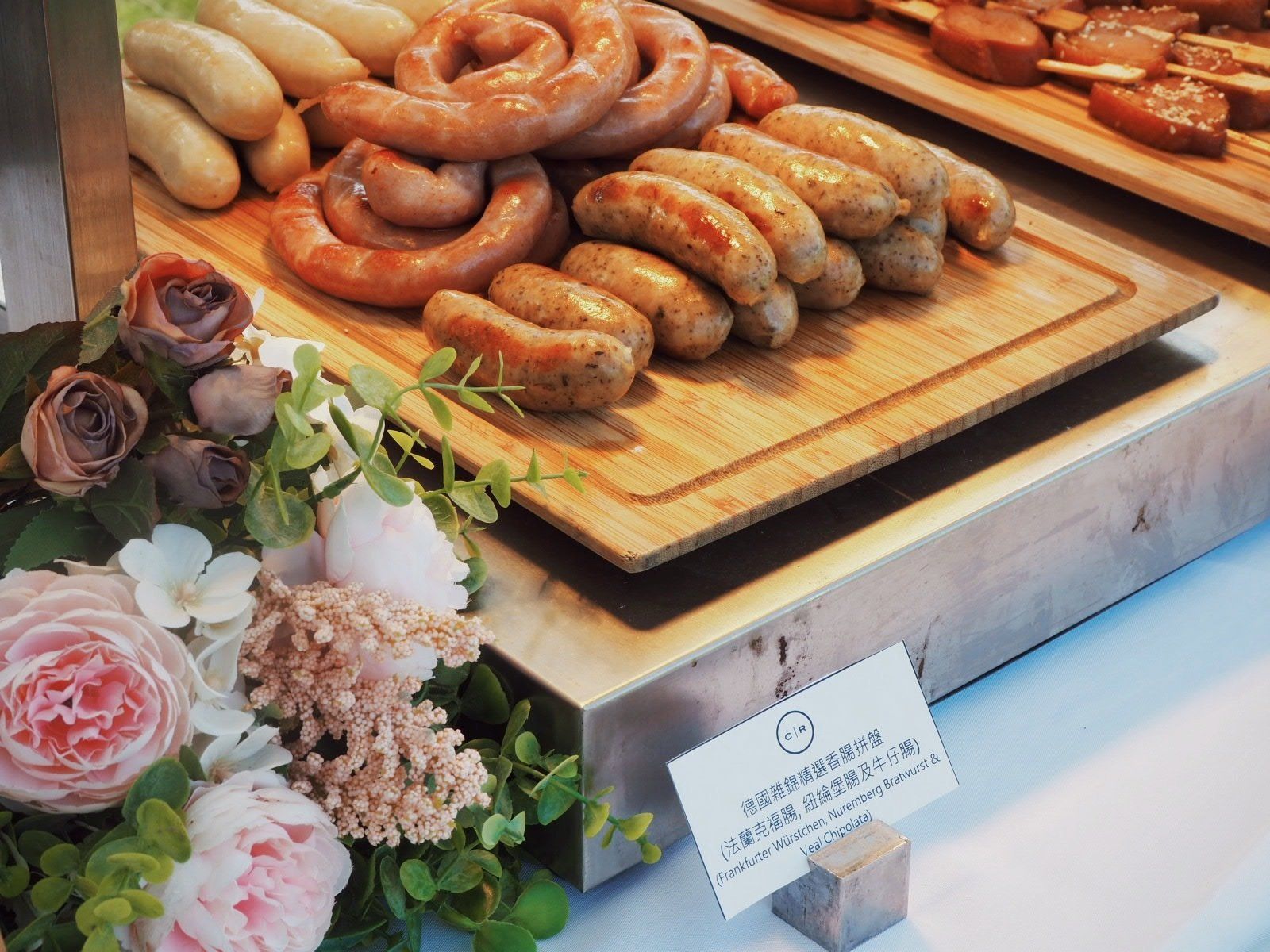 Assorted sausages on wooden boards; flowers in the foreground.