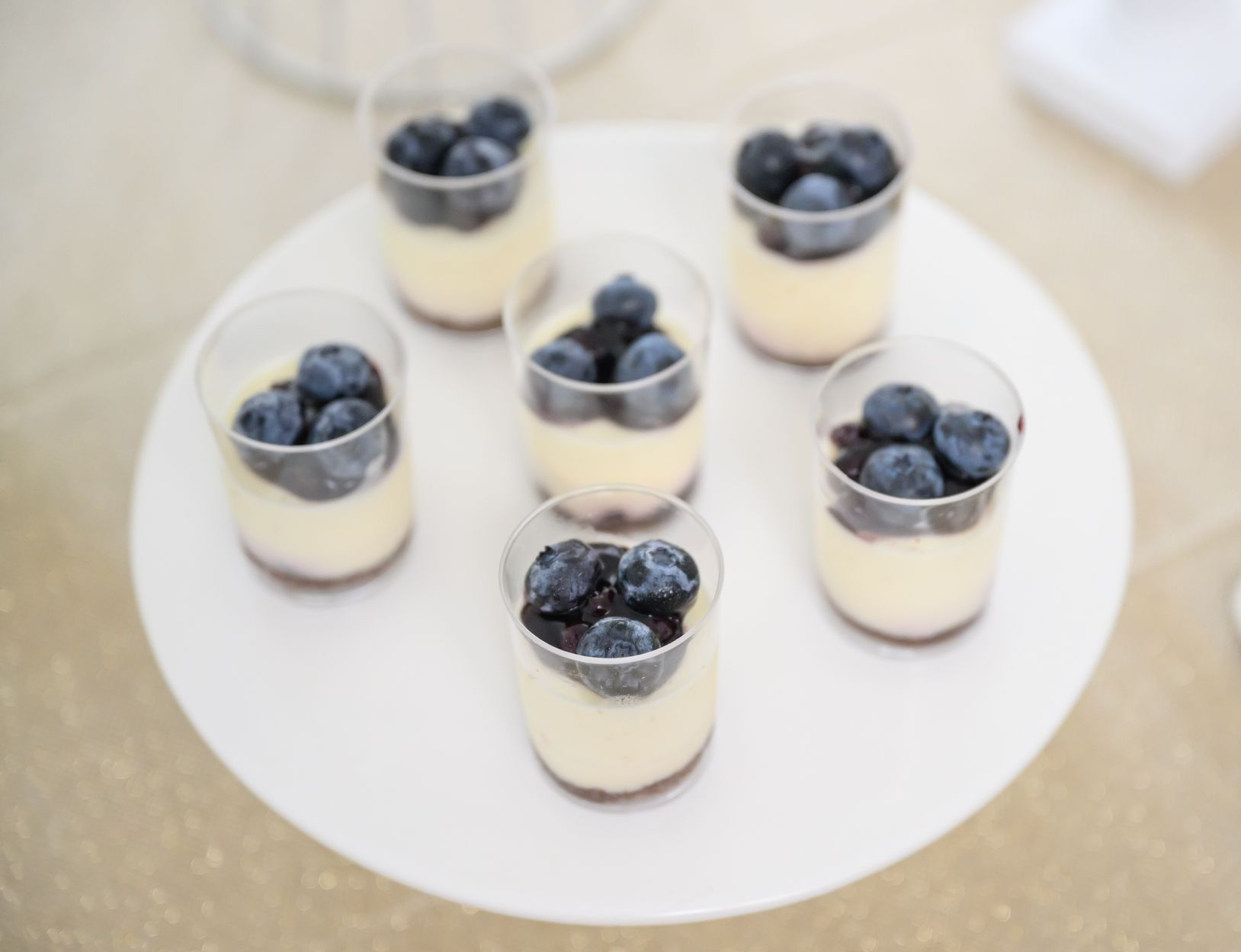 Six blueberry parfaits in clear cups on a white plate.