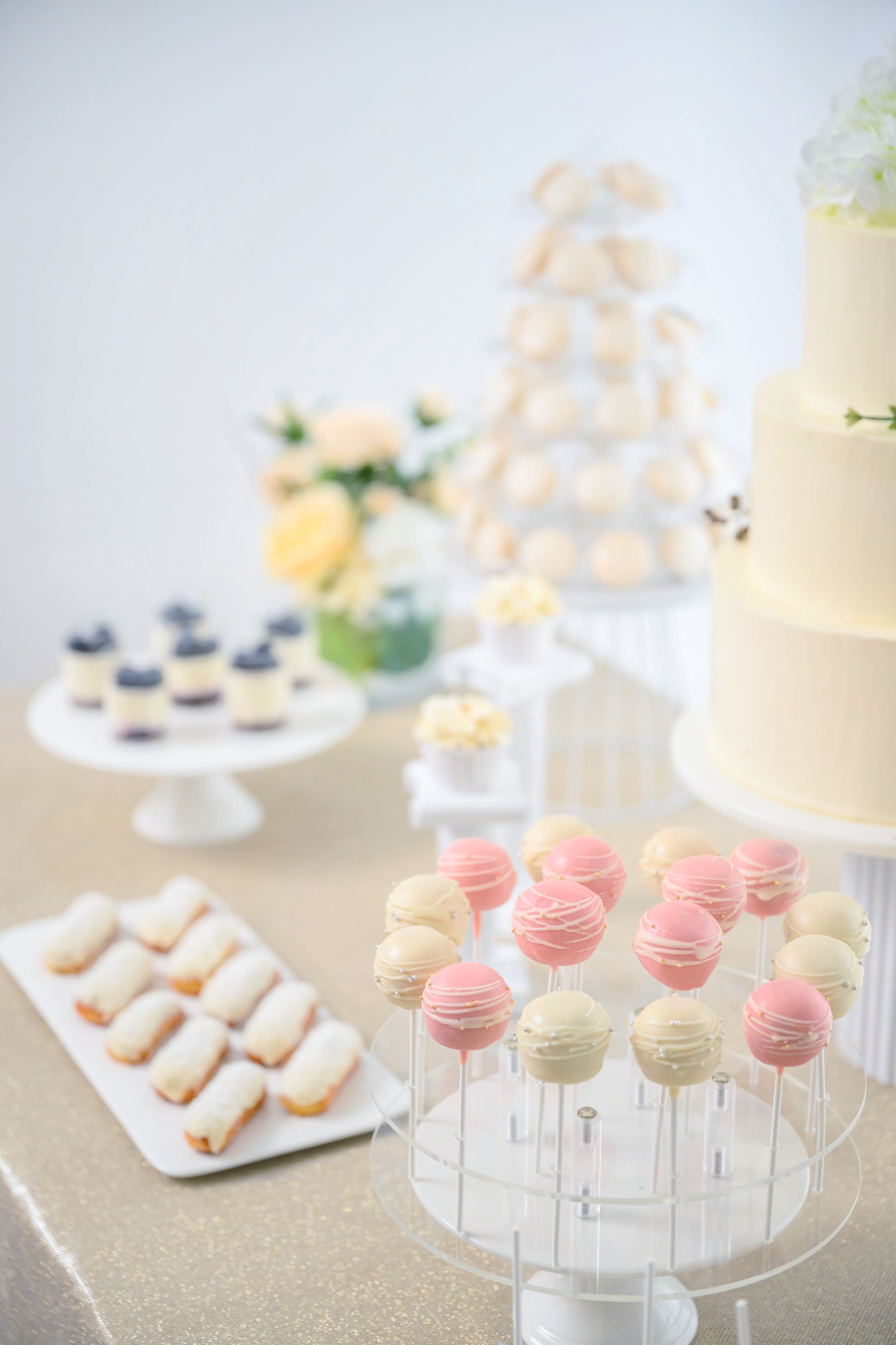 Dessert table with cake pops, a tiered cake, and other treats in a light-colored setting.