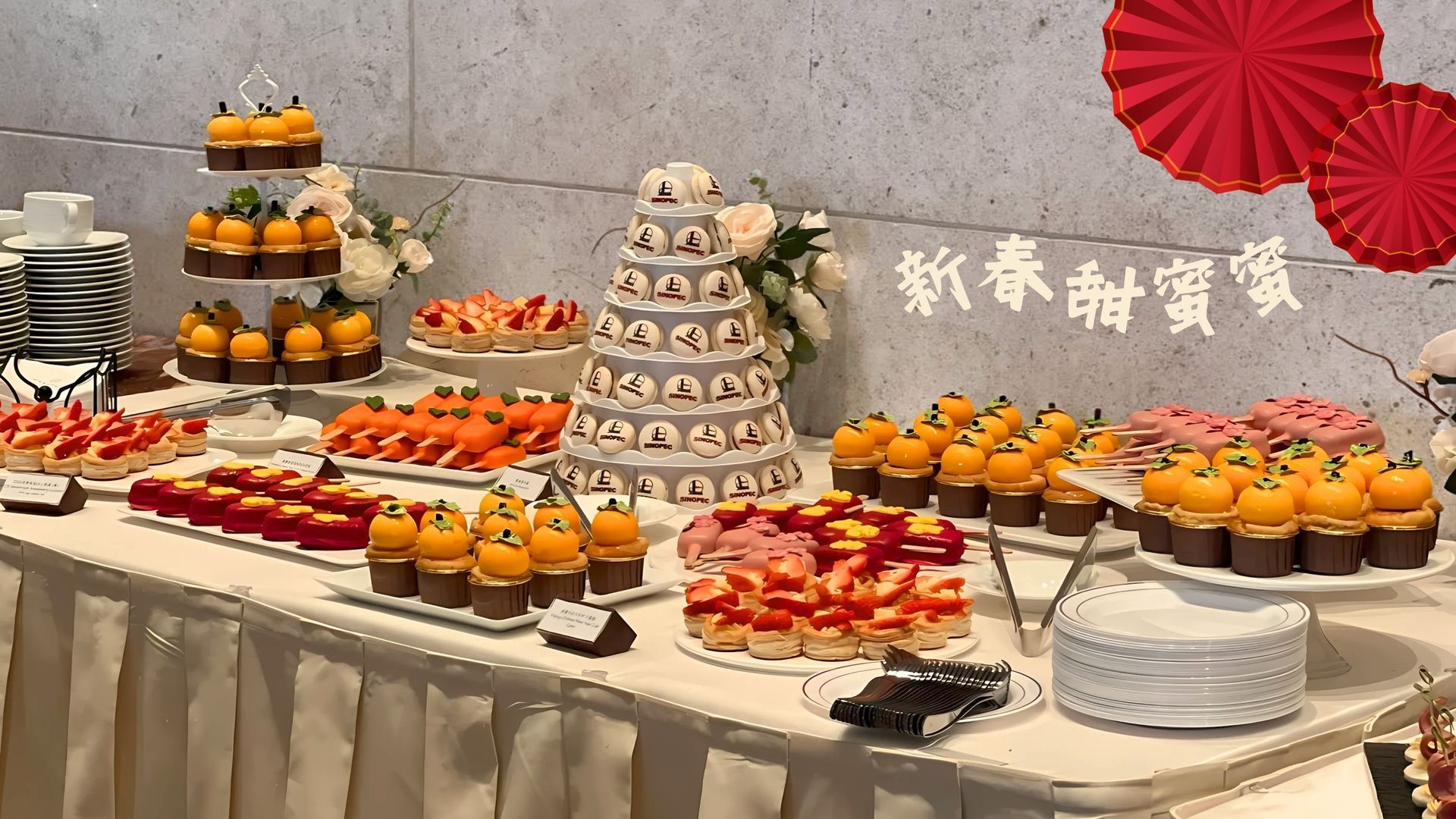 Dessert table: cupcakes, cakes, pastries, oranges, and red decorations for a celebration.