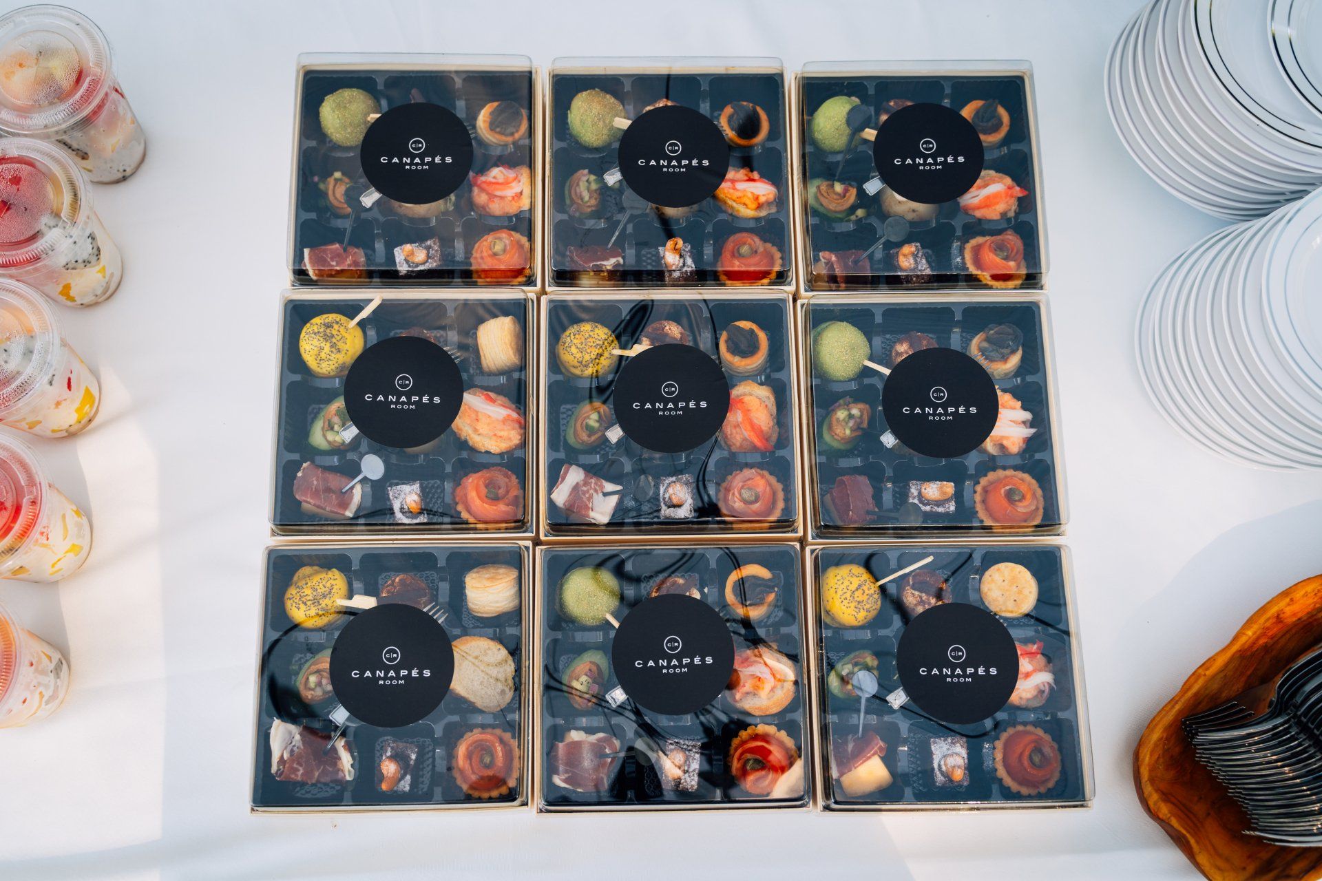 Nine boxes of assorted colorful treats, stacked. Beside them are drinks and plates.