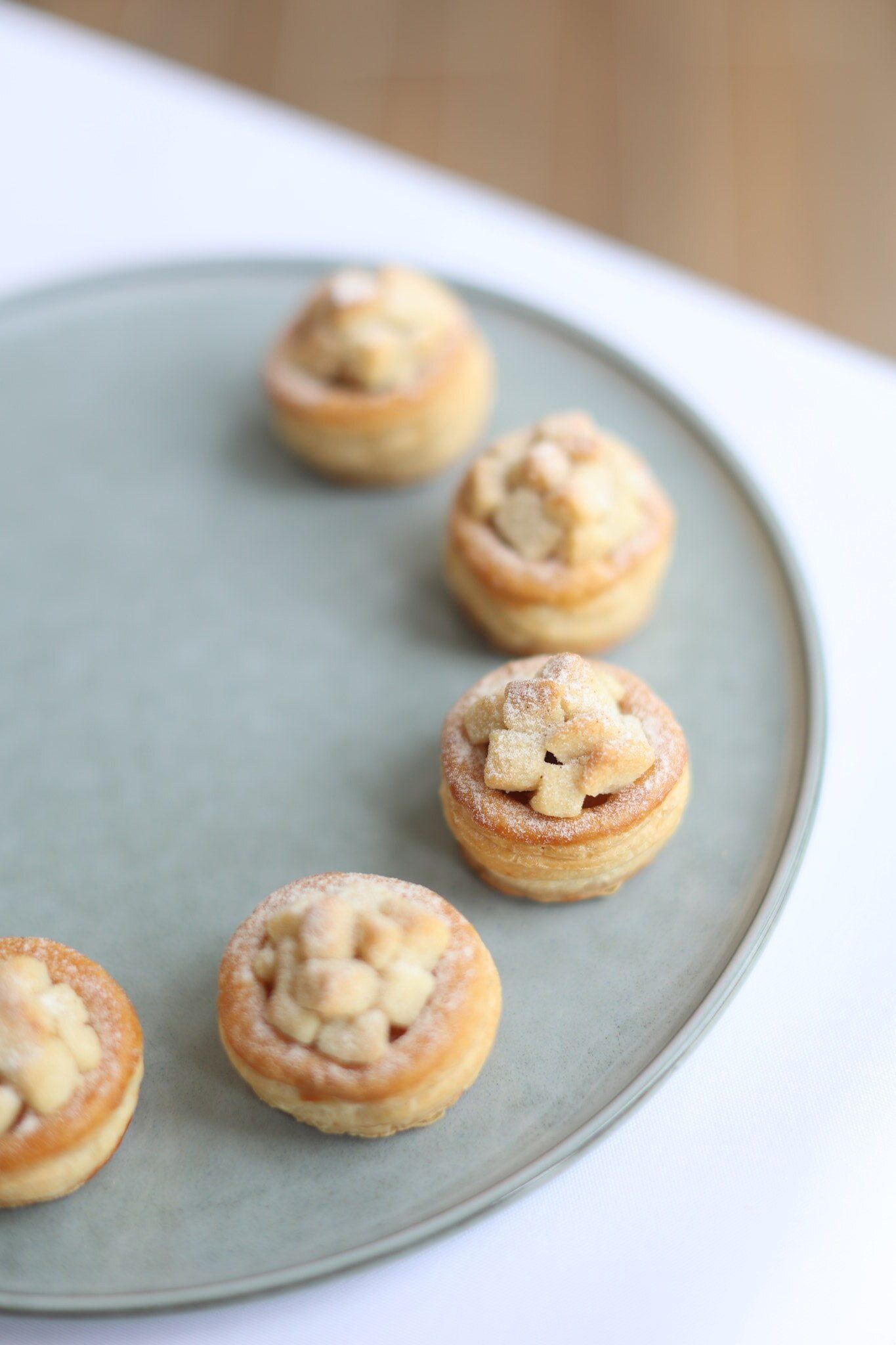 Mini apple pies arranged on a blue-grey plate; white surface in background.