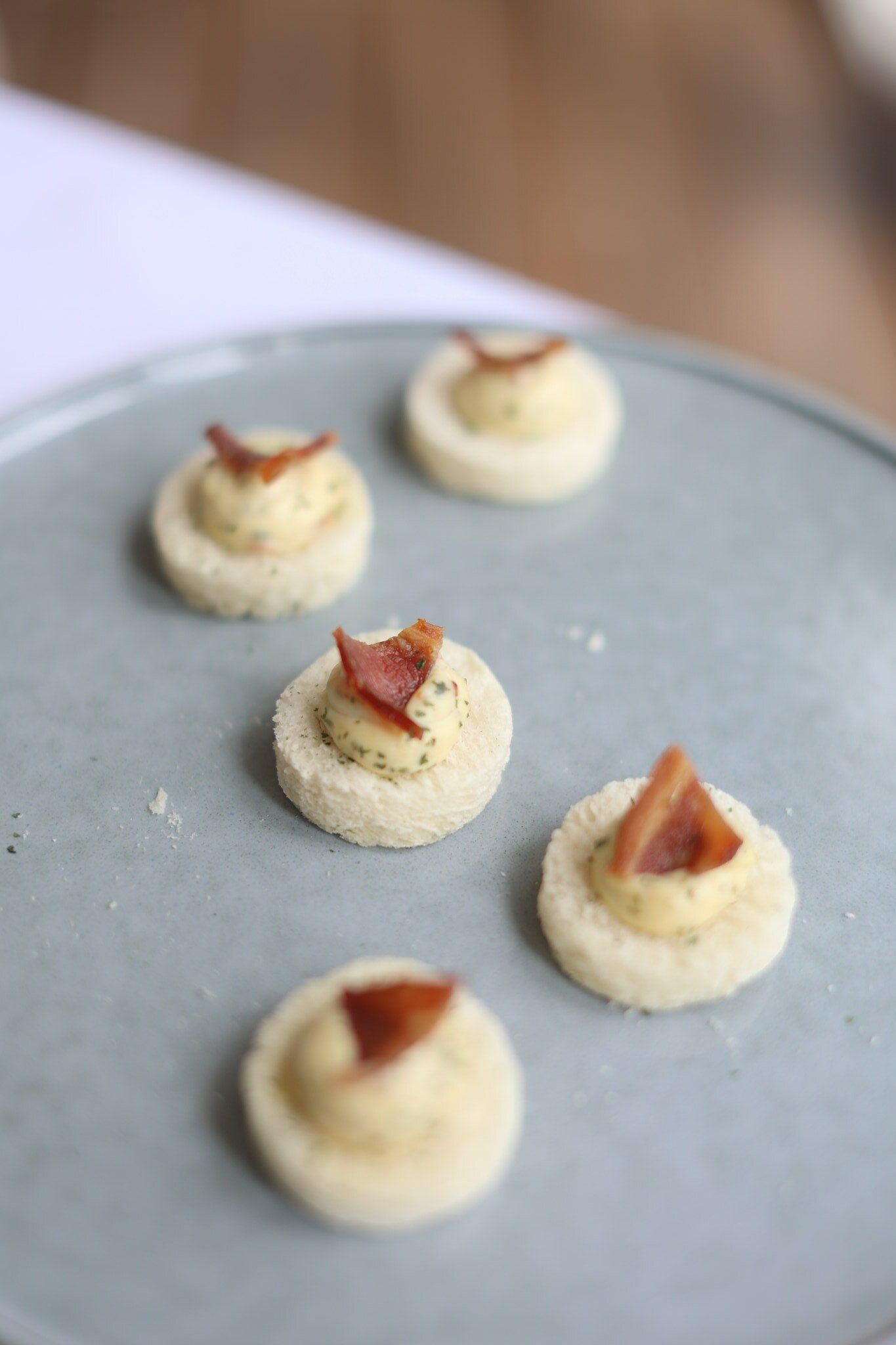 Small, round appetizers with creamy topping and bacon on a light blue plate.