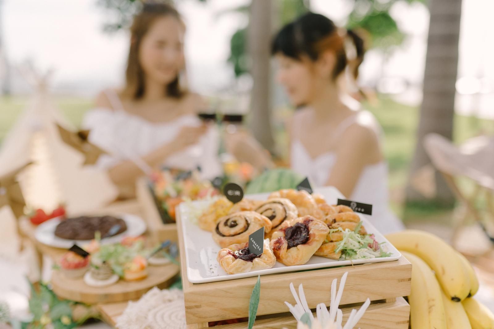 Two women enjoying a picnic outdoors with food displayed on a wooden crate.