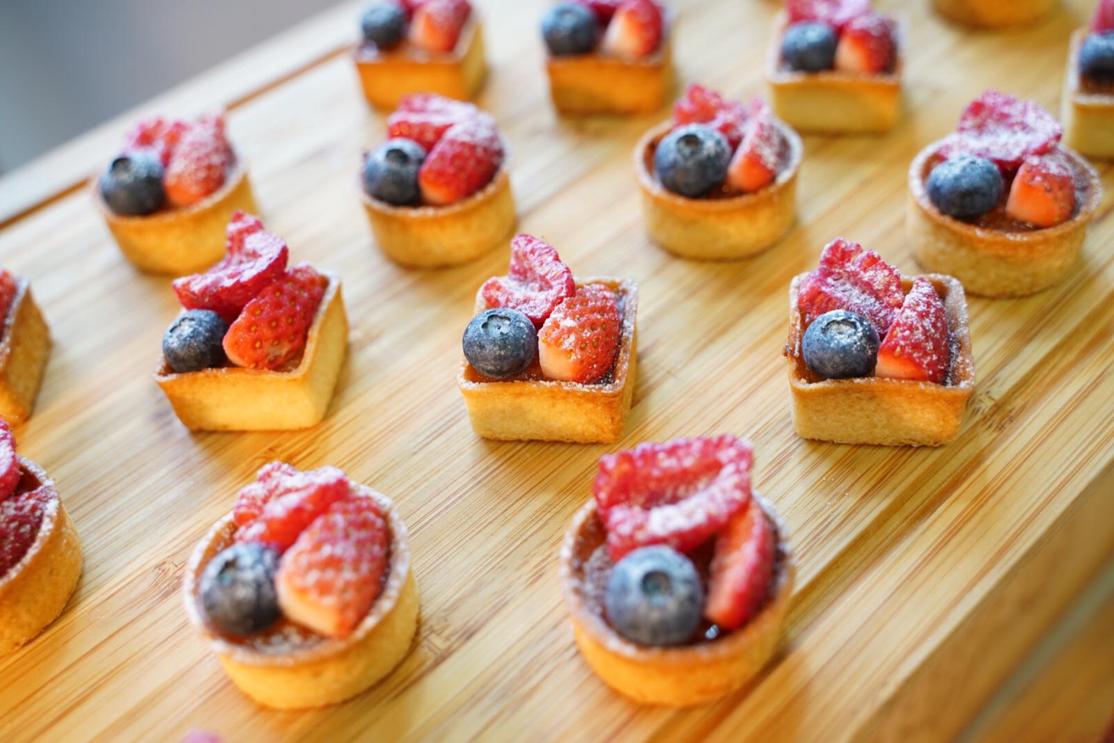 Small fruit tarts with strawberries and blueberries on a wooden tray.