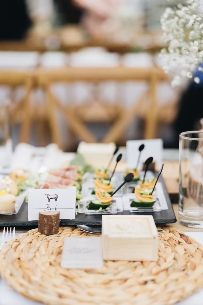 Charcuterie board on a table with appetizers, place setting, and decorative flowers.