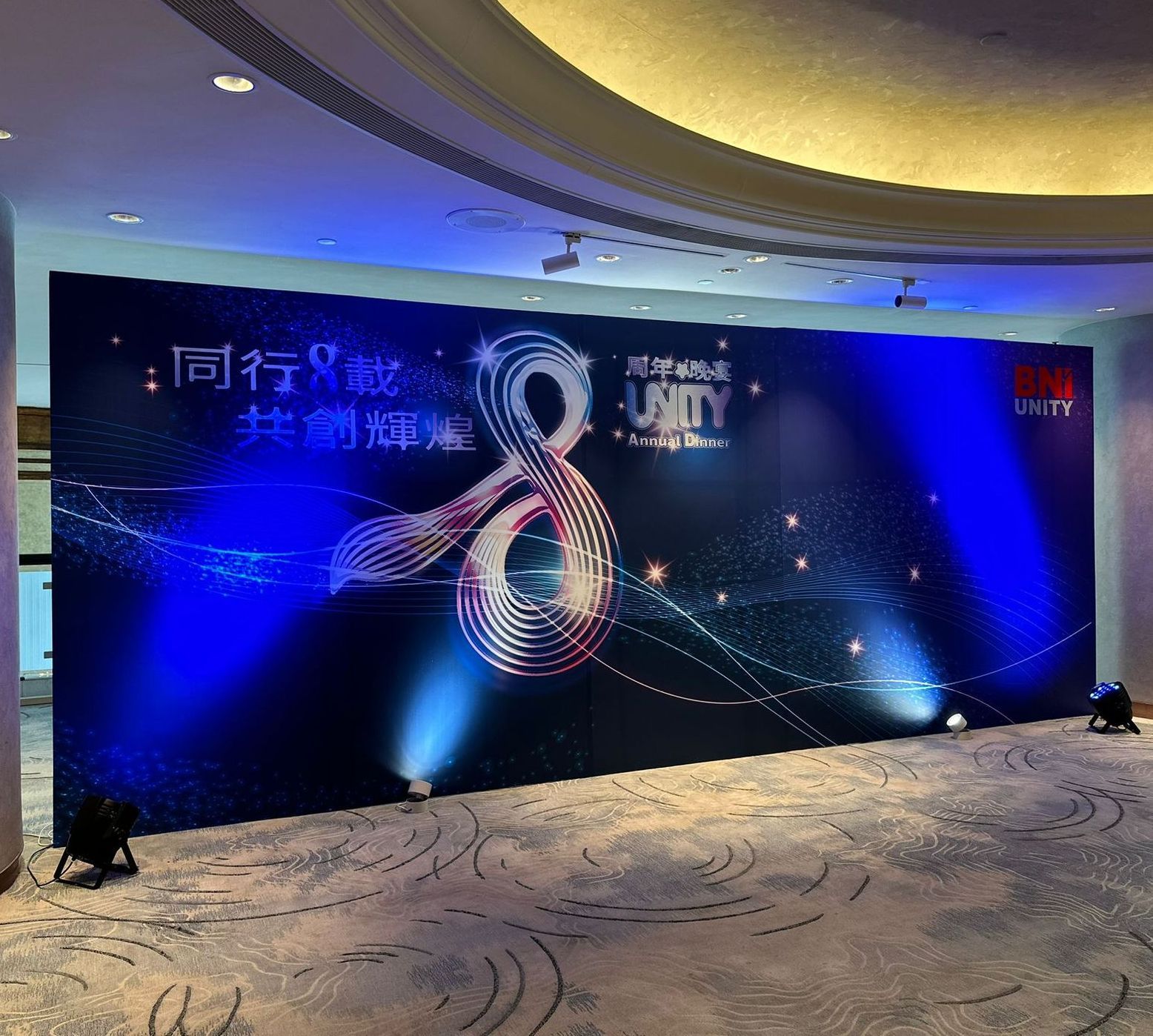 Blue-lit stage backdrop with the number 8 and text in Chinese characters, lights, and logo for an event.