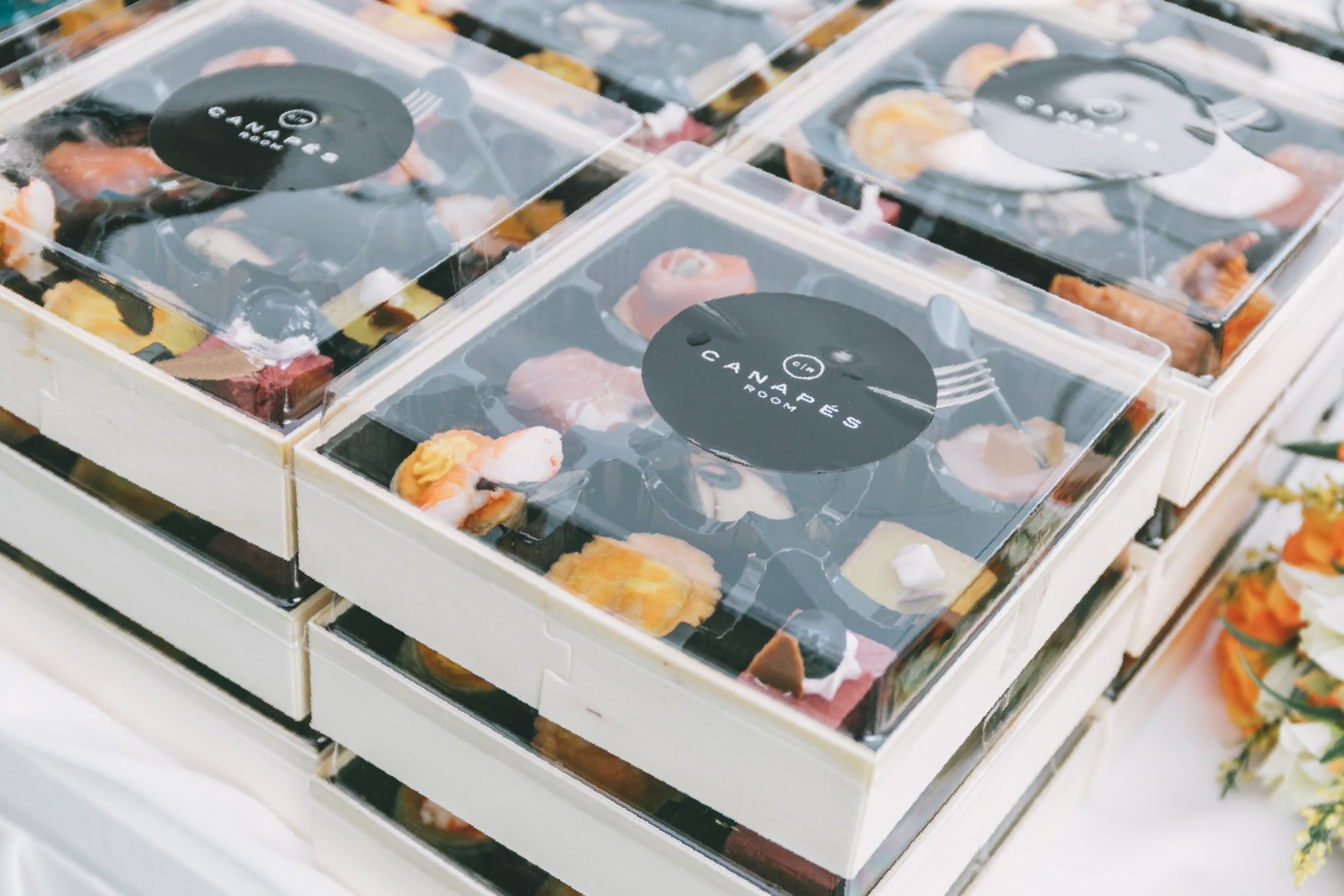 Boxes of gourmet food, each with a clear lid and sticker. Stacked on a white surface, ready to be served.