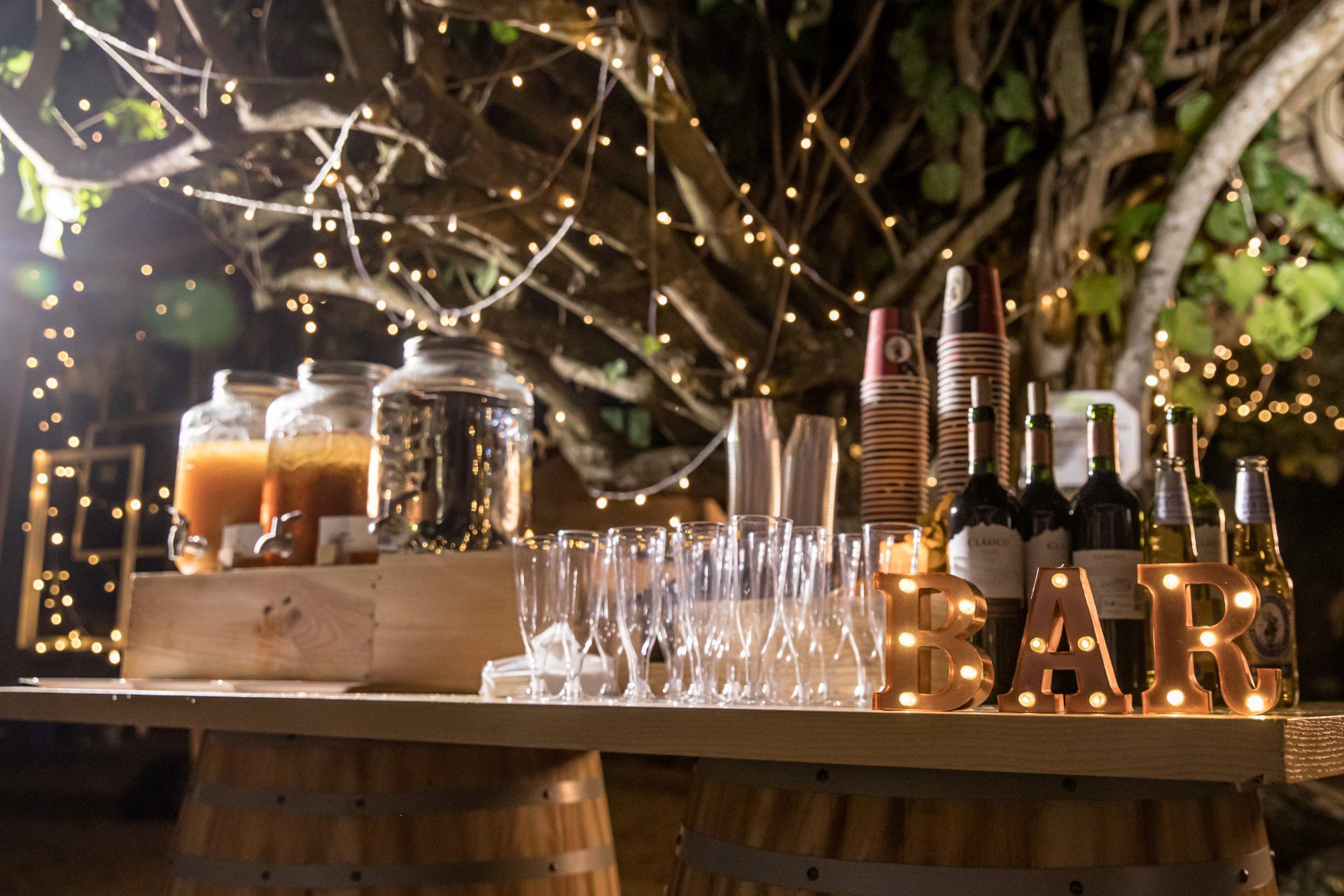 戶外酒吧提供飲料、玻璃杯和亮著的「BAR」標誌；頭頂上有一串串燈。