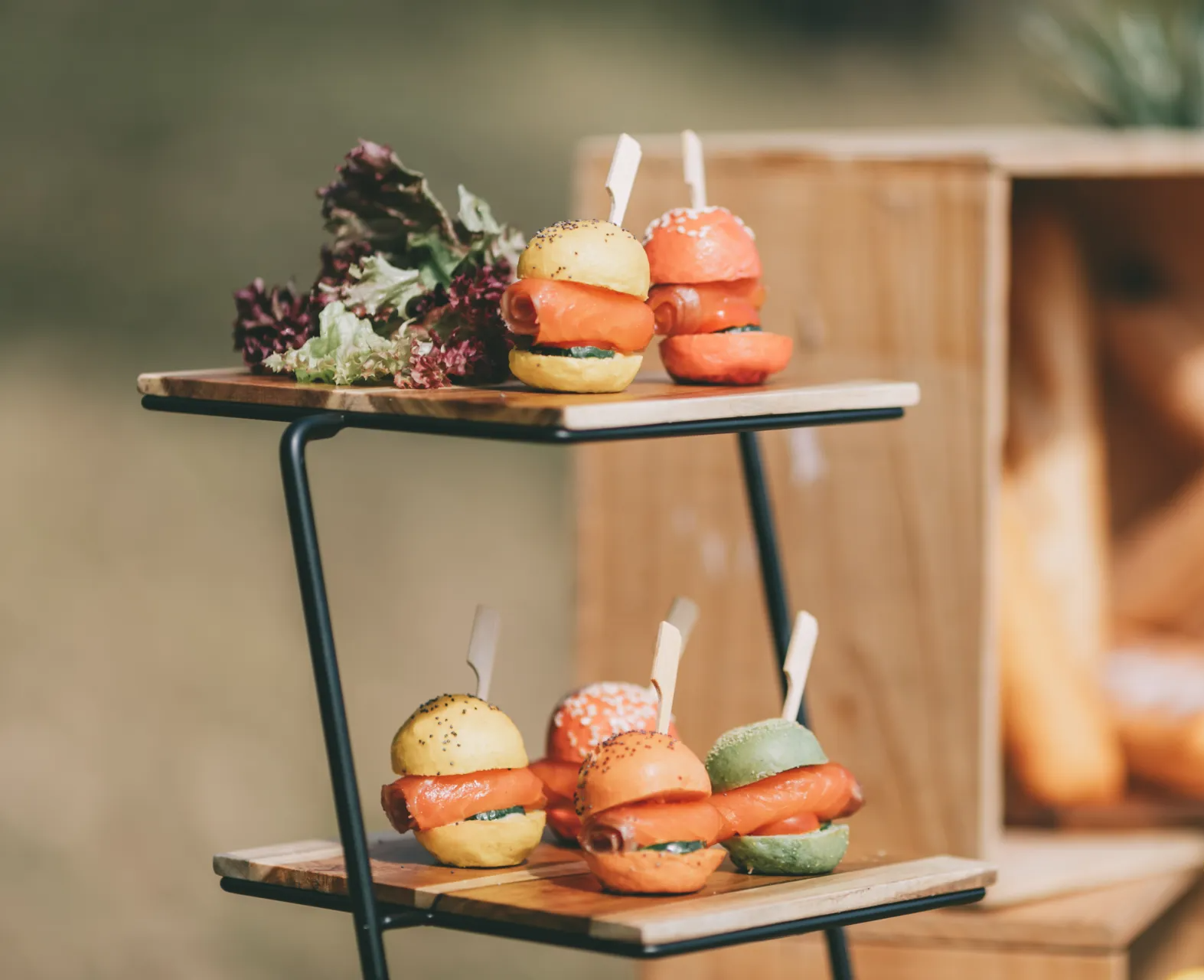 Mini sandwiches on a tiered serving stand; yellow, orange, and green buns with salmon.