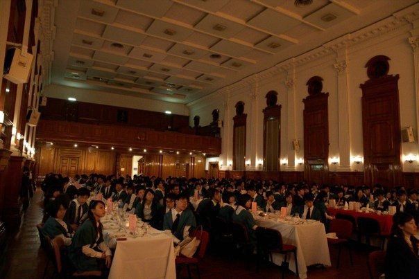 寬敞的正式大廳，桌旁坐滿了人。許多人穿著綠色制服。燈光昏暗。