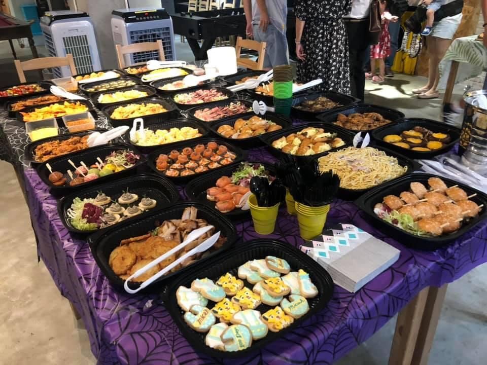 Table laden with various dishes, at an event; purple tablecloth with spider web pattern.