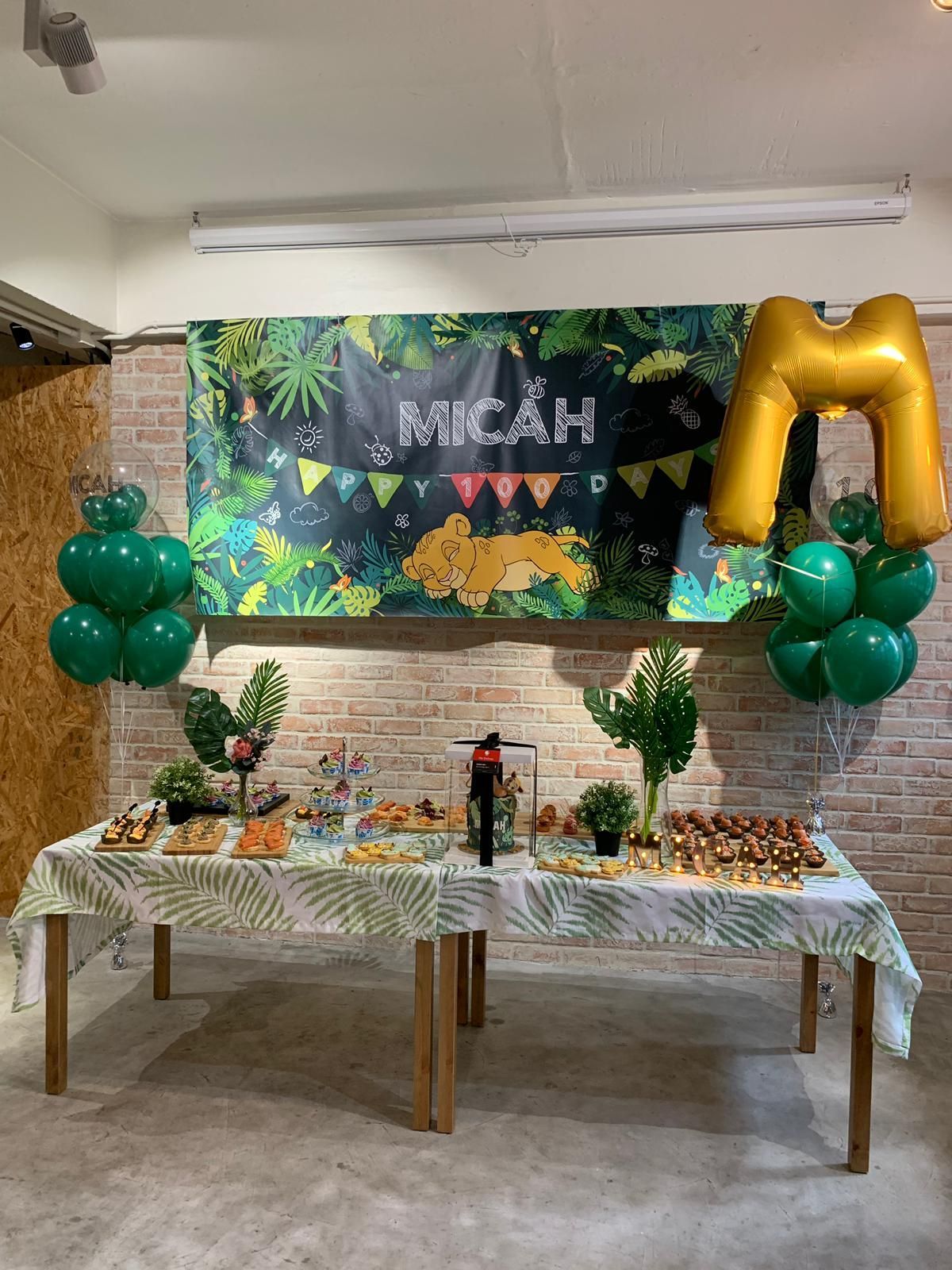 A decorated table for a party with food and balloons; banner says