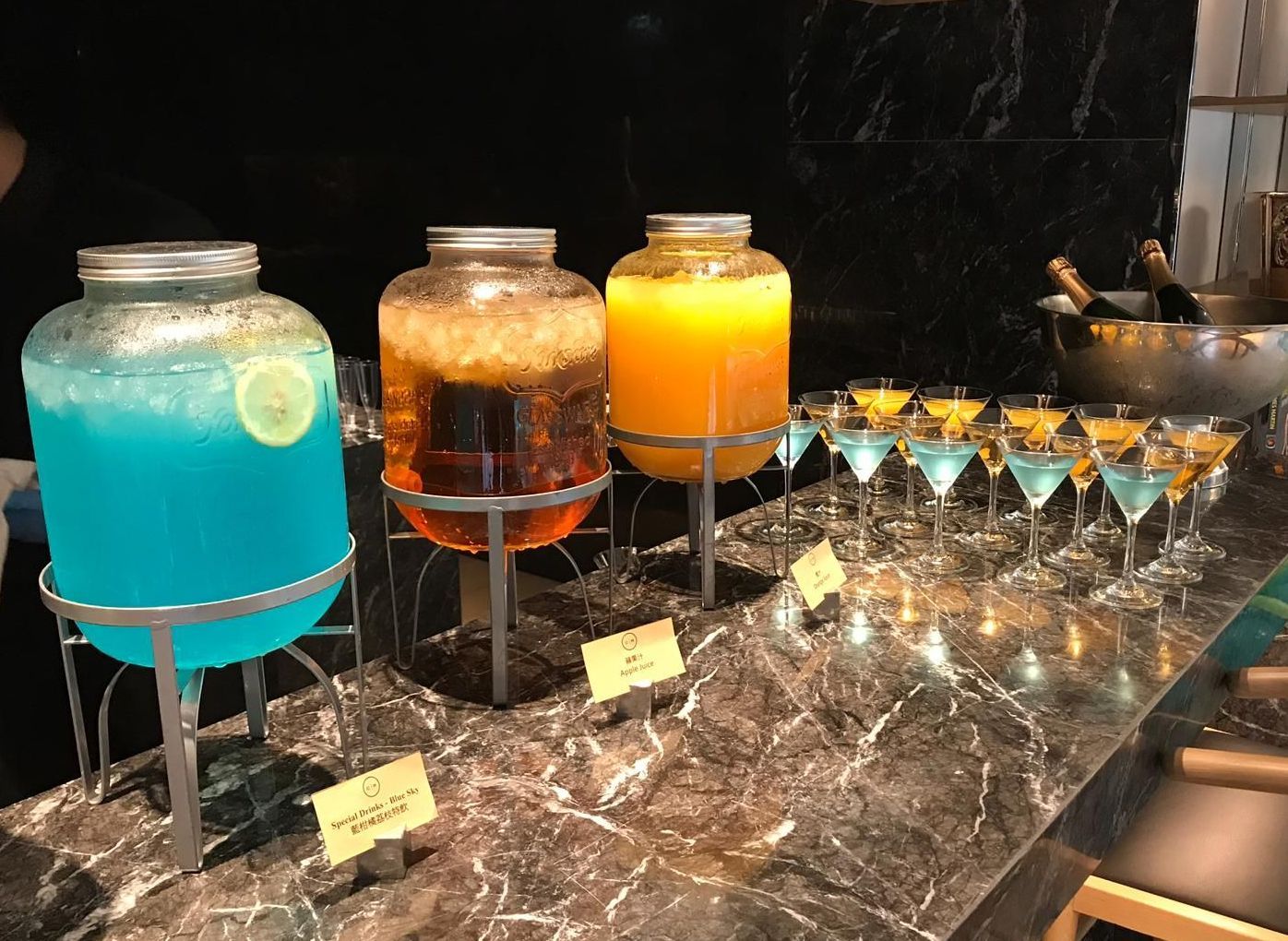 Buffet with blue, brown, and orange drinks in glass jars, and cocktails in glasses.