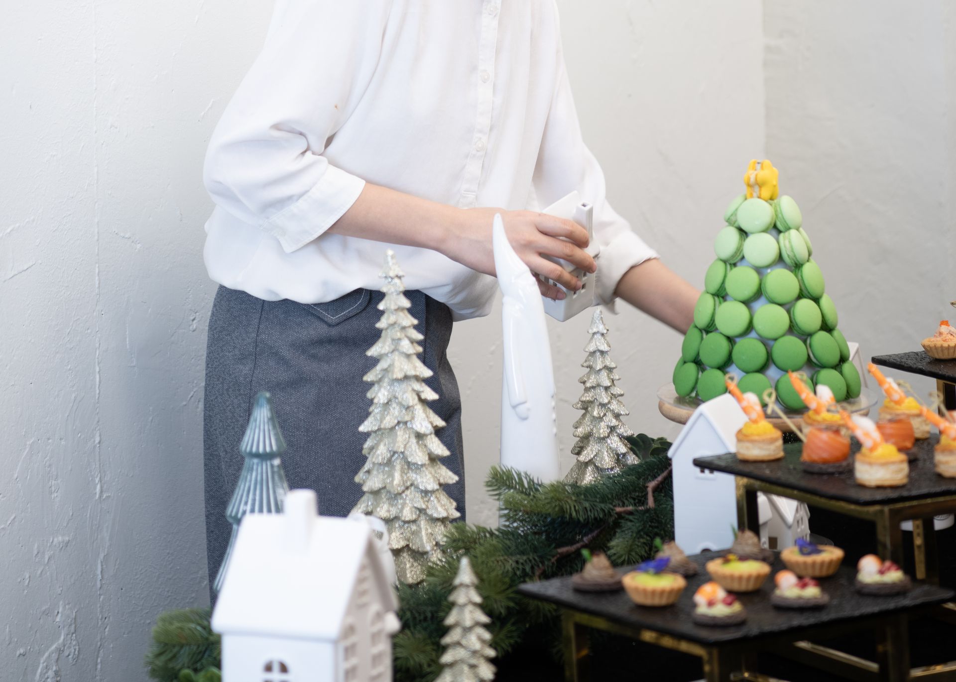 Person arranging desserts on a table decorated with Christmas trees and houses.