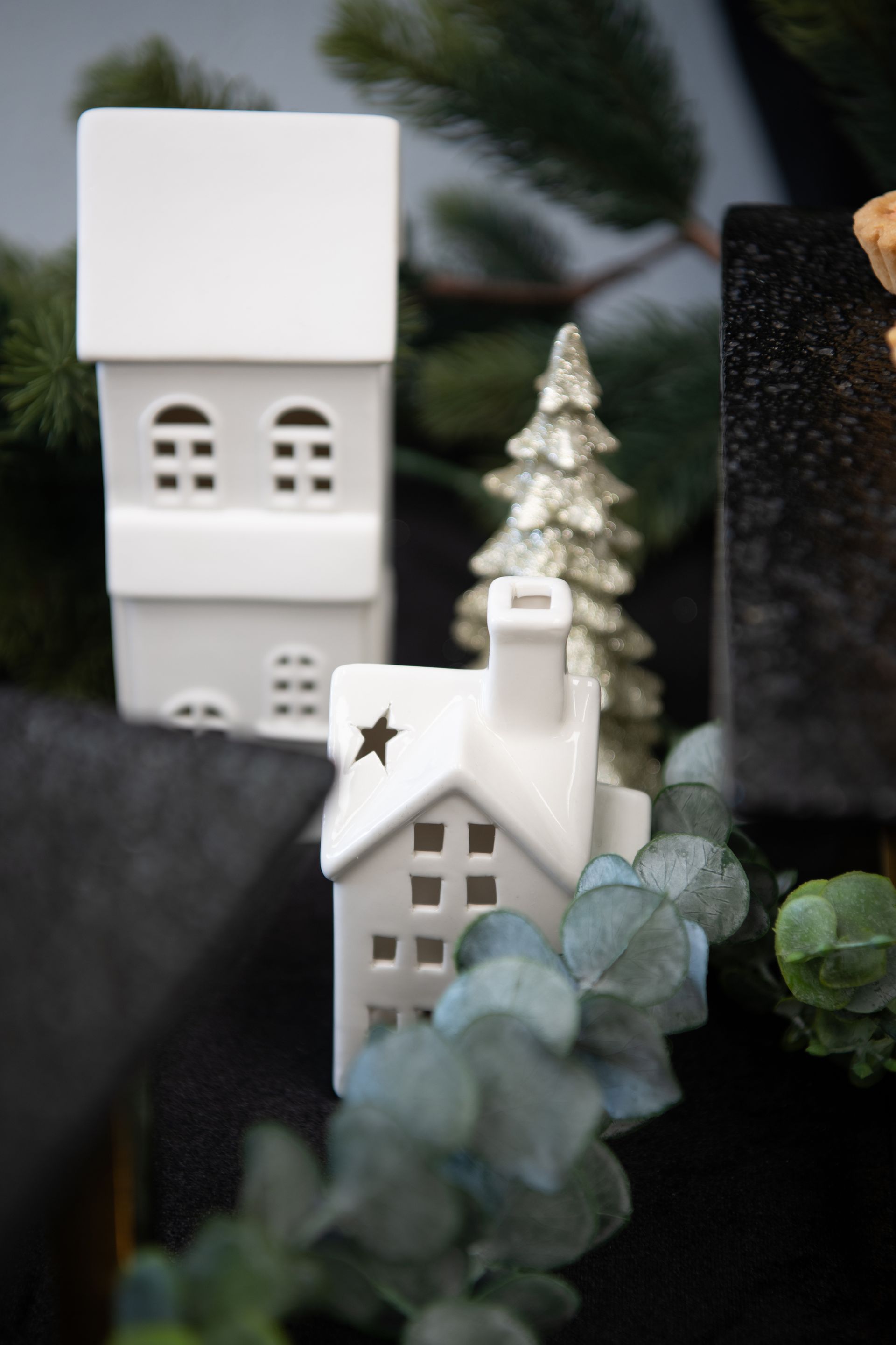 White ceramic houses and a silver Christmas tree surrounded by greenery.