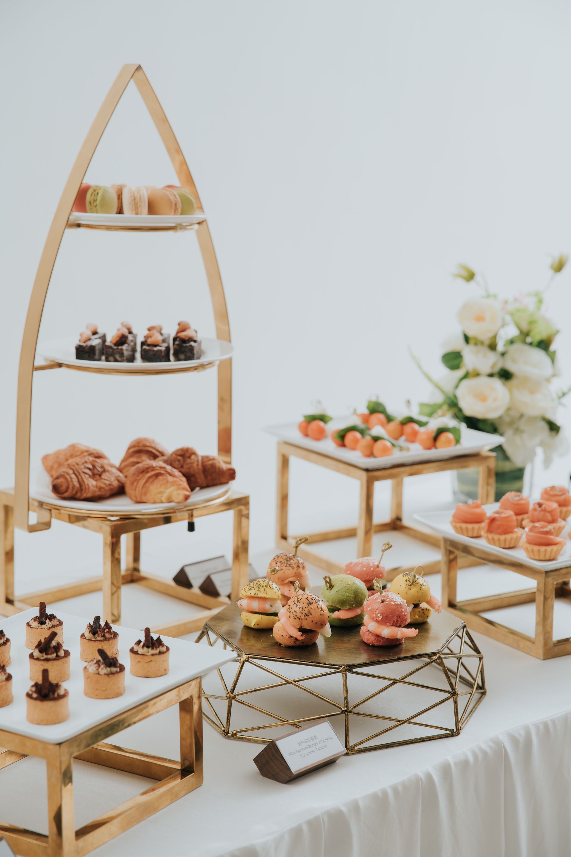 甜點桌上擺放著各種糕點和鮮花,白色桌布上。