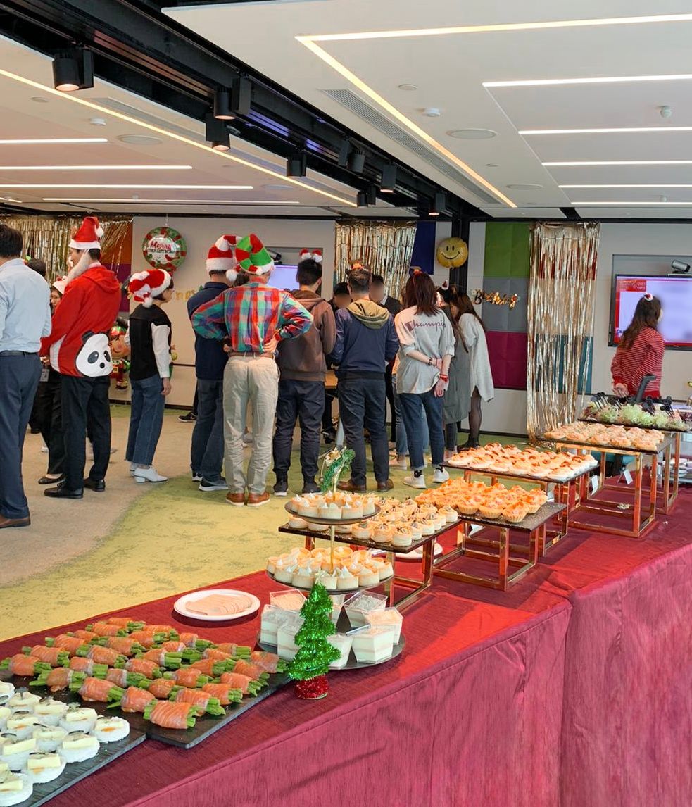 Office holiday party with buffet table and people wearing festive hats.
