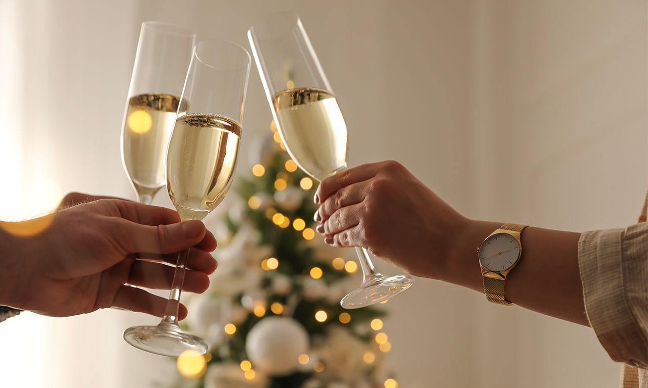 Three champagne flutes clinking, filled with bubbly, in front of a decorated Christmas tree.
