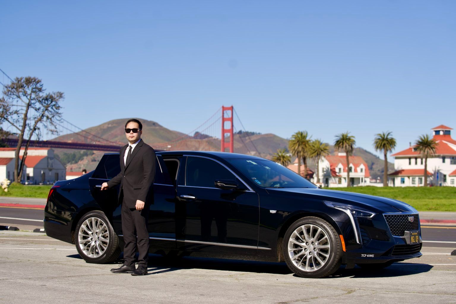 A man in a suit and tie is standing next to a black car.