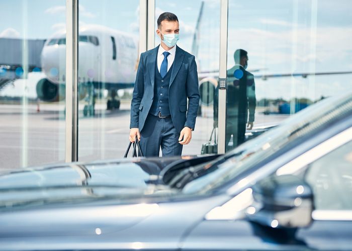 A man wearing a mask is walking towards a car at an airport.