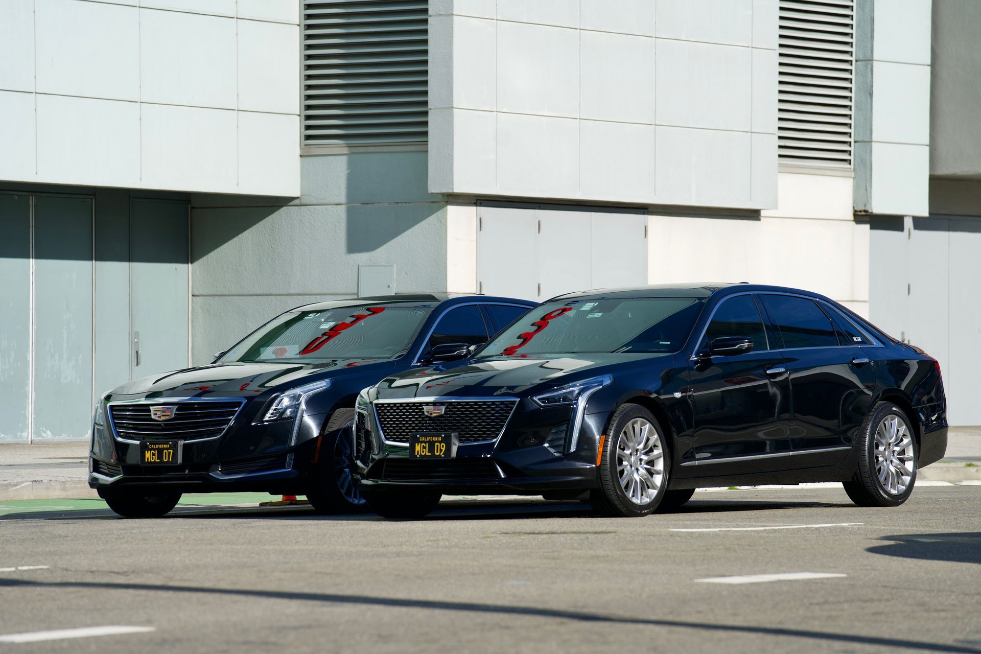 Two black sedans parked in front of a modern building on a sunny day.