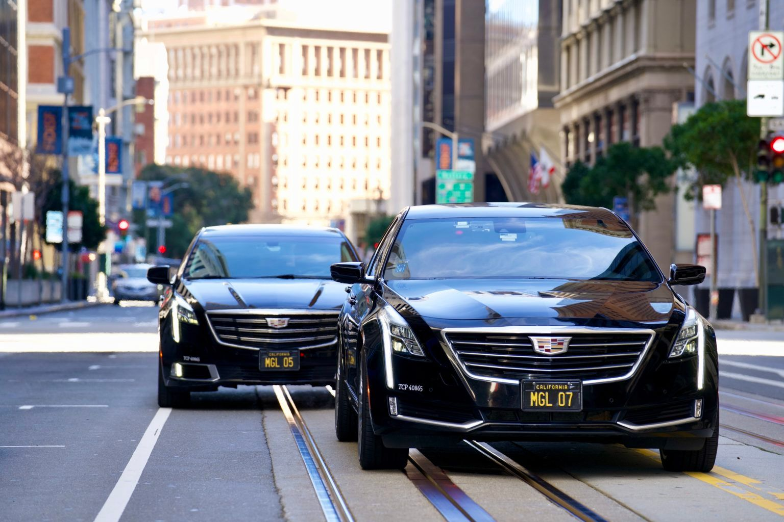 Two black cars are driving down a city street.
