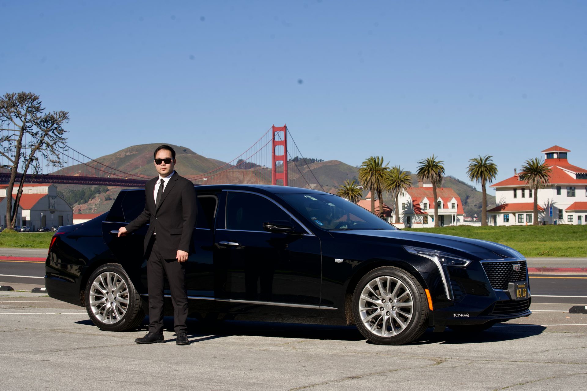 Man in suit beside black Cadillac sedan with the Golden Gate Bridge in the background.