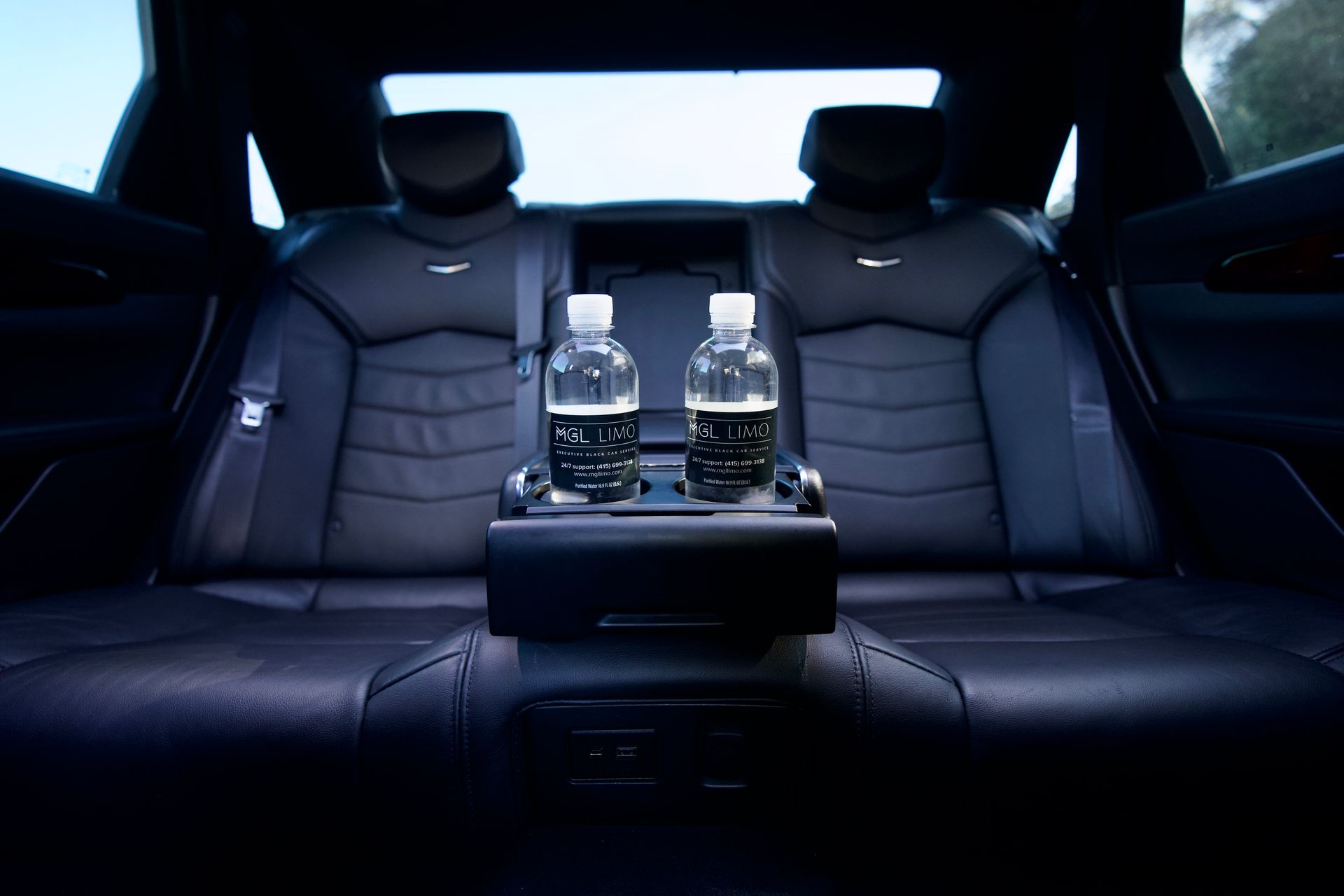 Interior car back seat with two water bottles in a center console, black leather seats.