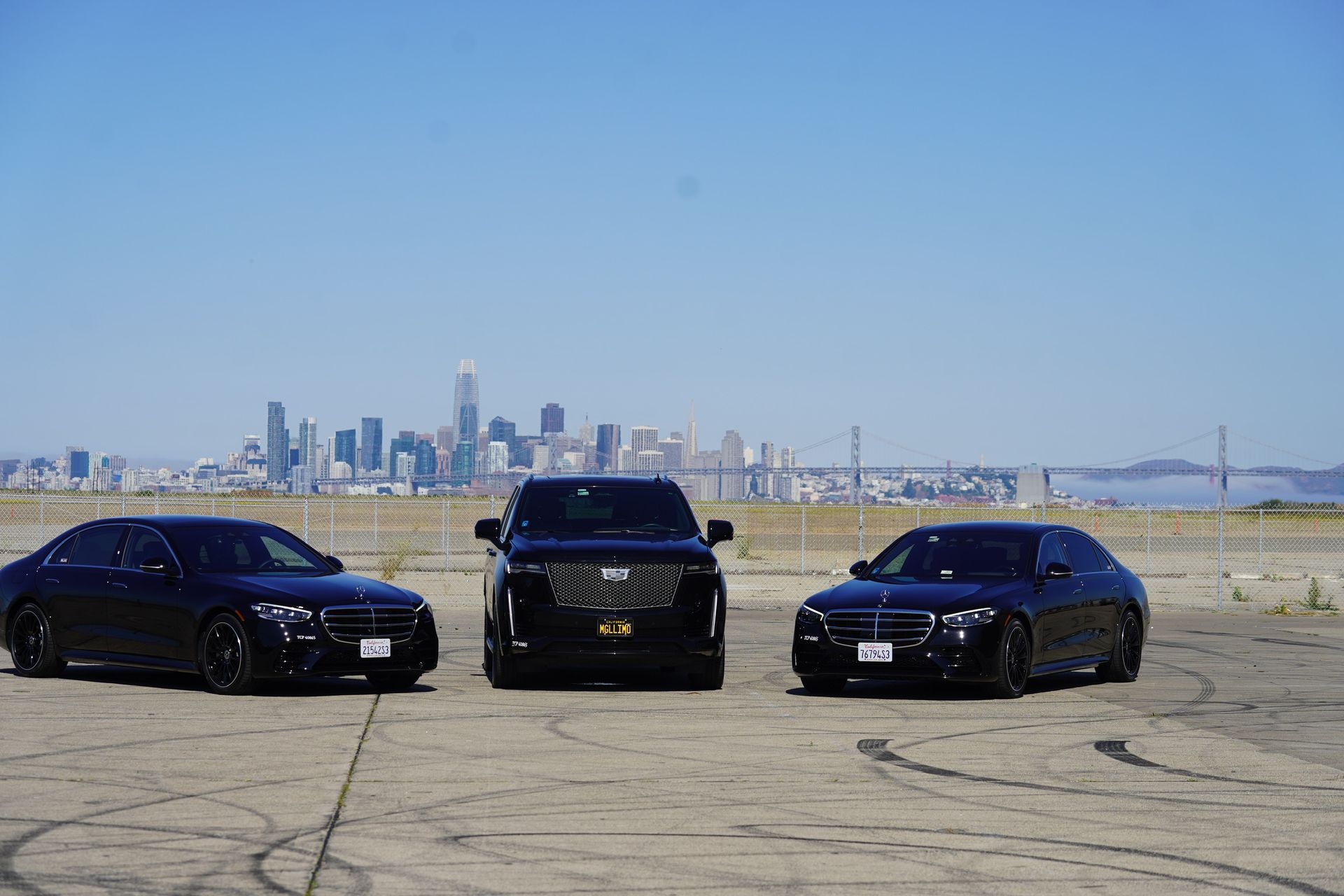 Three black cars parked outdoors, San Francisco skyline in the background.