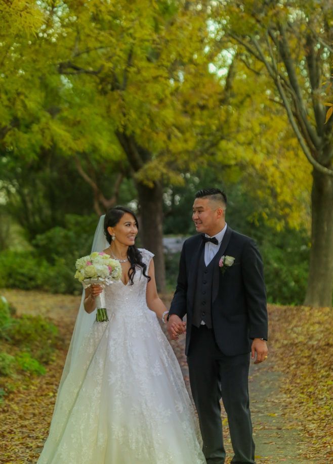 A bride and groom are walking down a path holding hands.