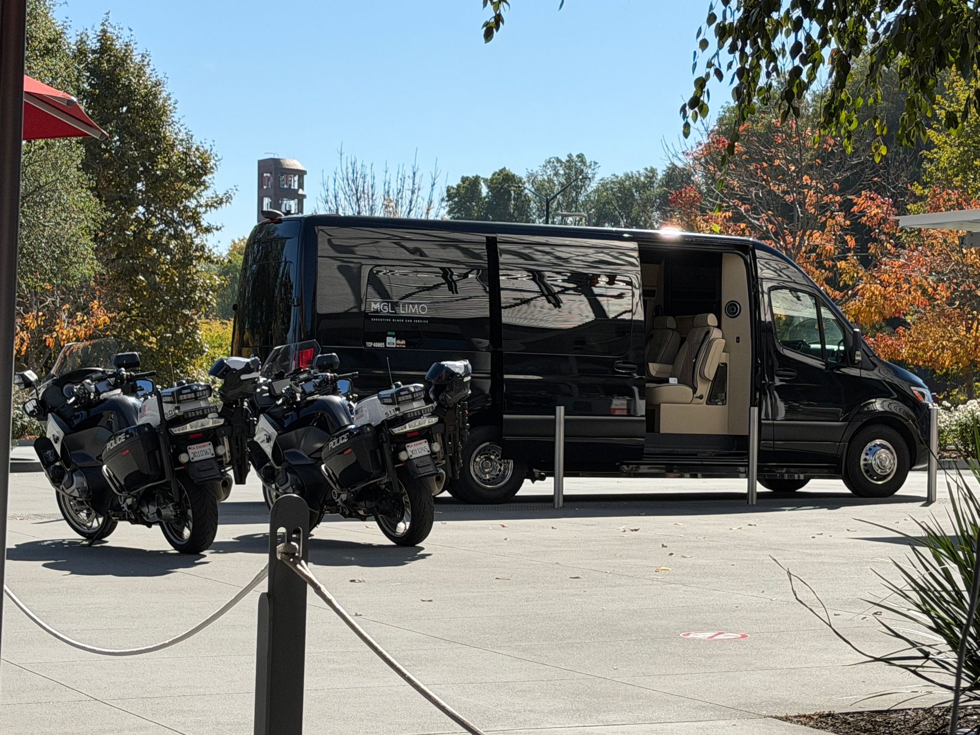 Black van with open side door and two motorcycles parked nearby. Outdoors, sunny day.