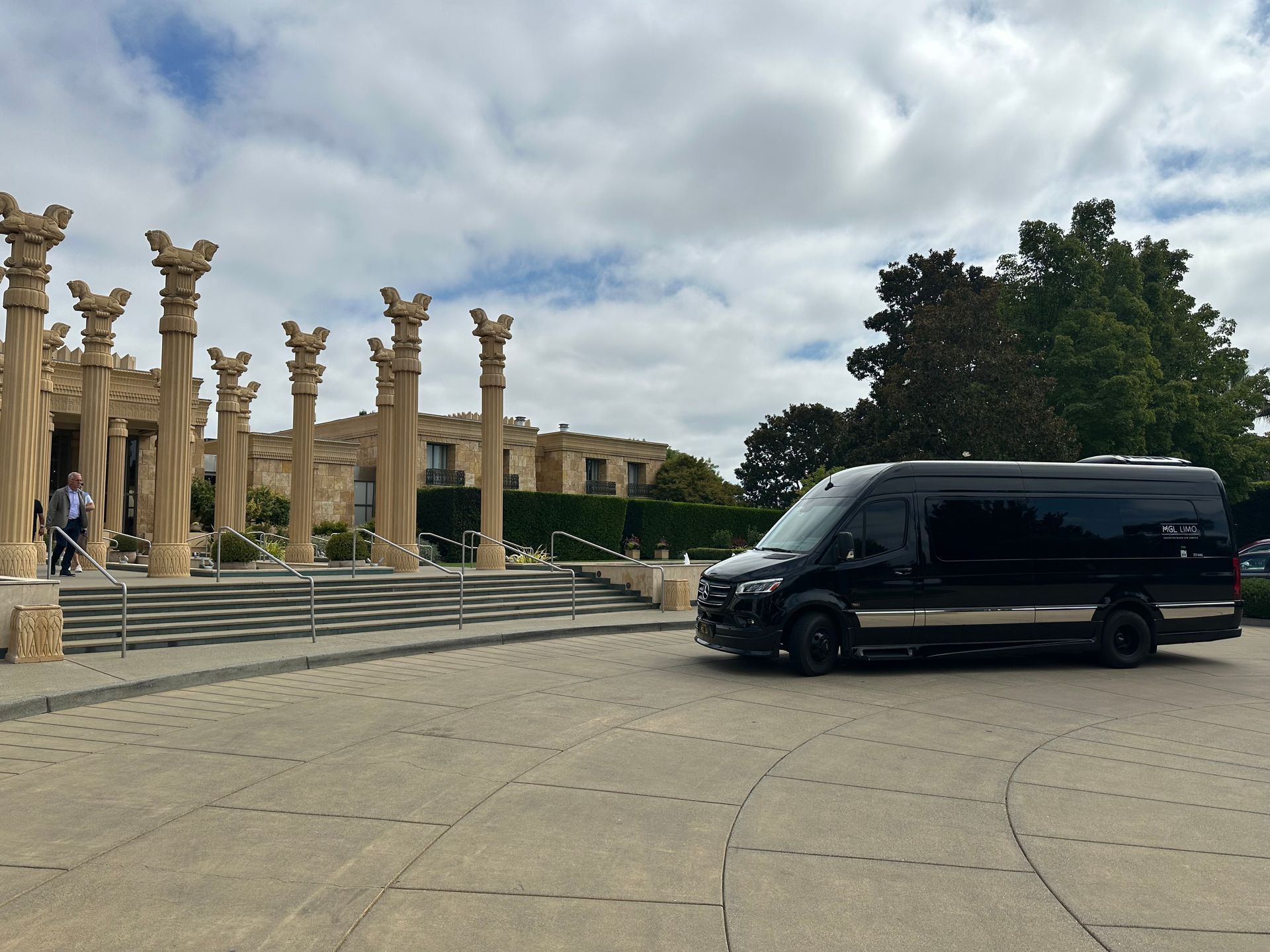 Black van parked near a building with columns and steps on a cloudy day.