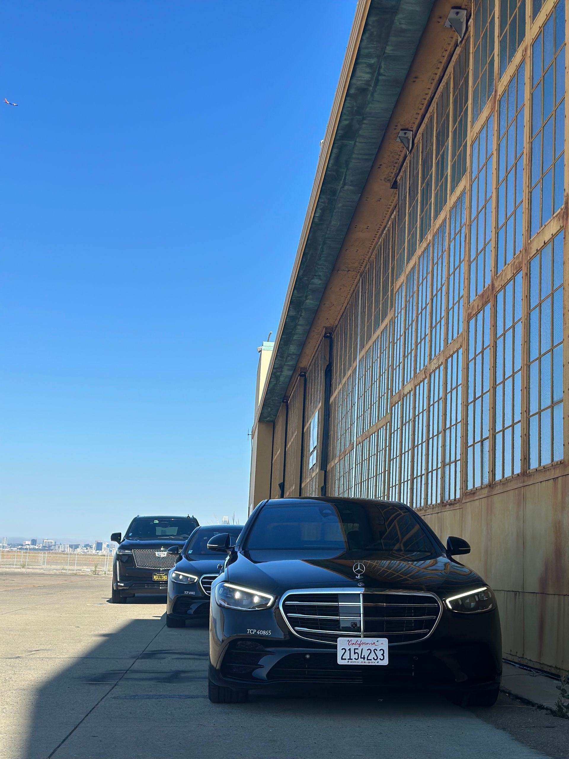Three black cars parked next to a large building under a bright blue sky.