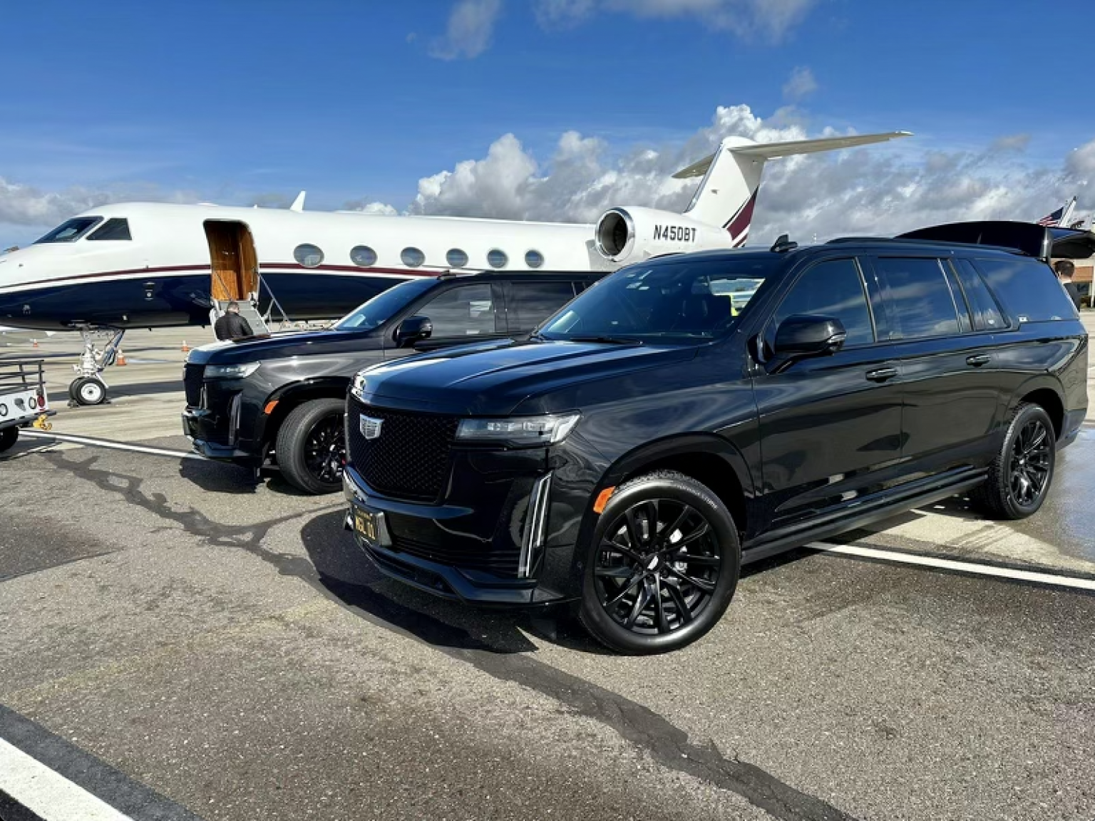 Two black cars are parked in front of a private jet.