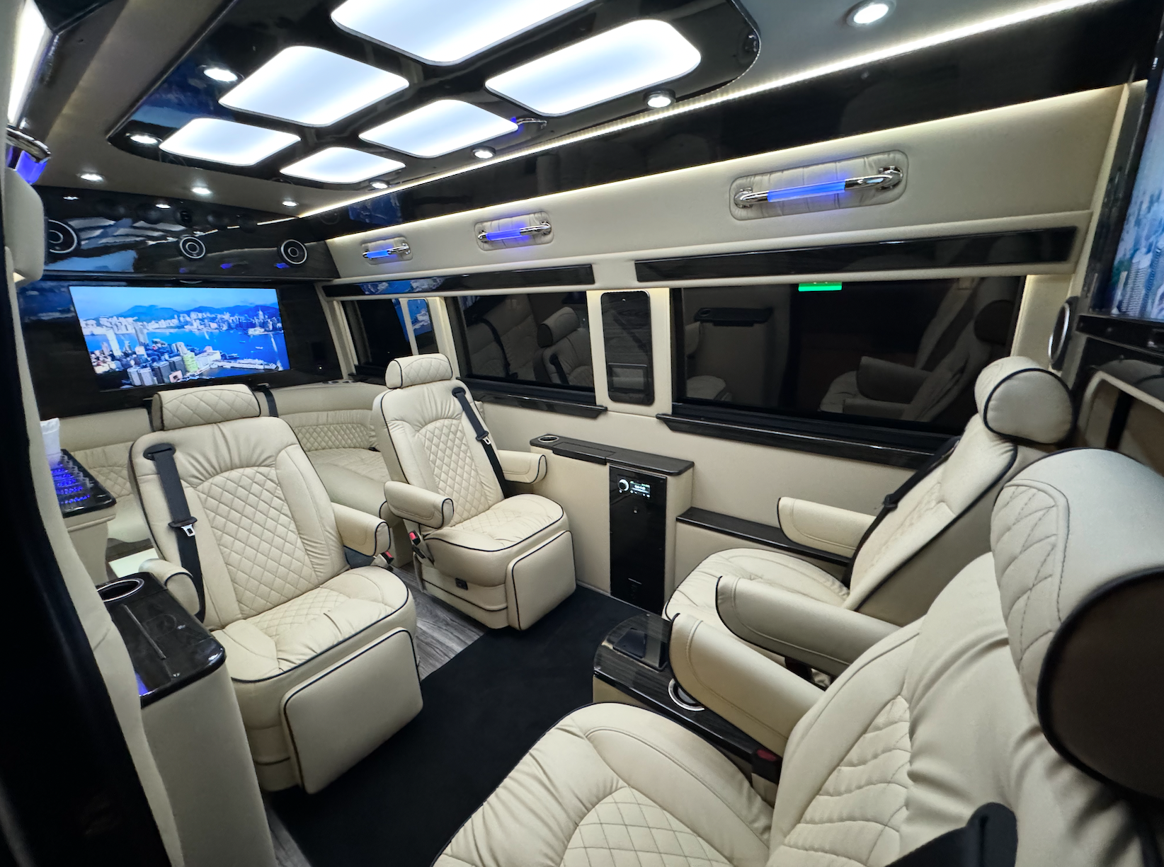 Interior of a luxury van with cream-colored leather seating, multiple screens, and ambient lighting.