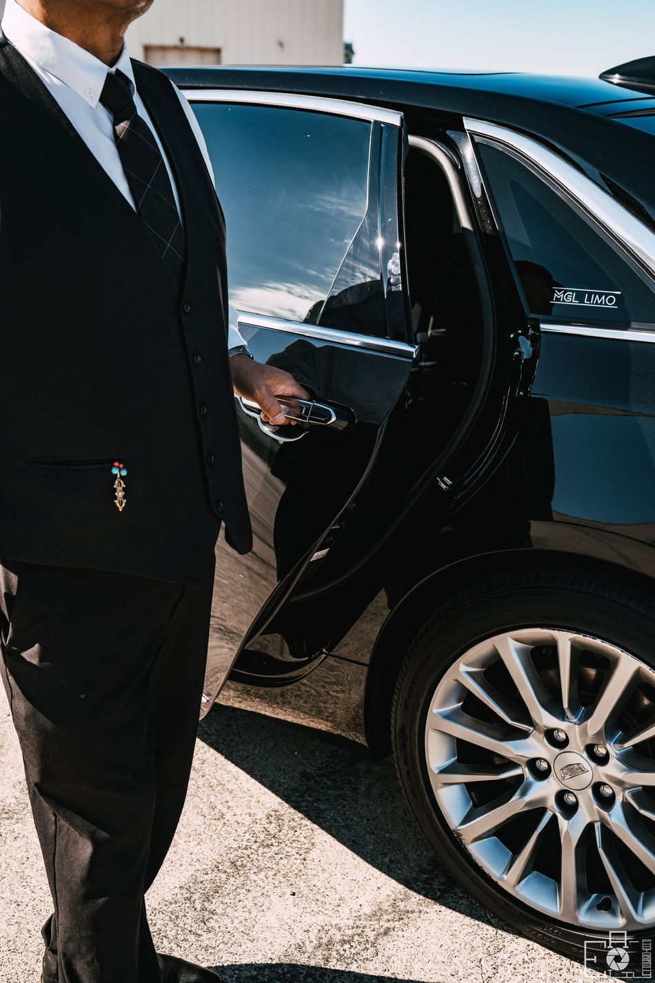 A man in a suit and tie is opening the door of a black car.