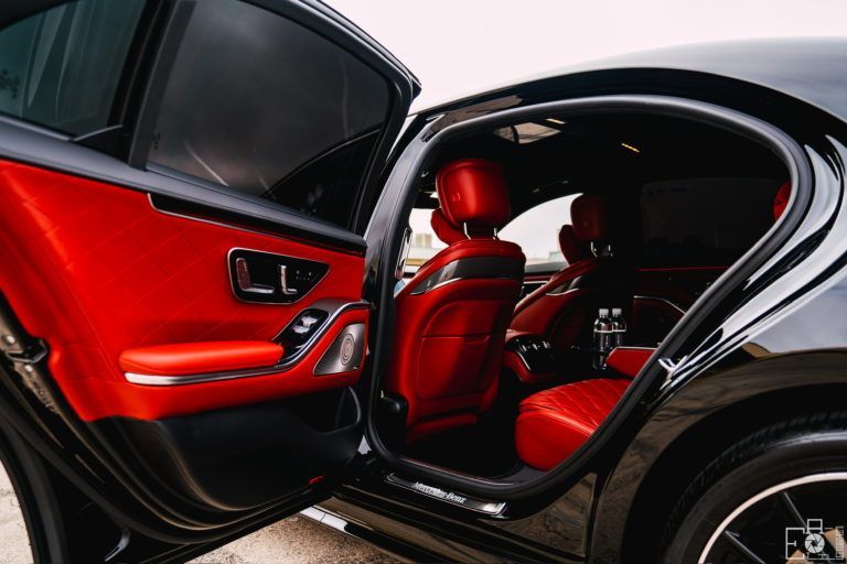The back seat of a black car with the door open and red seats.