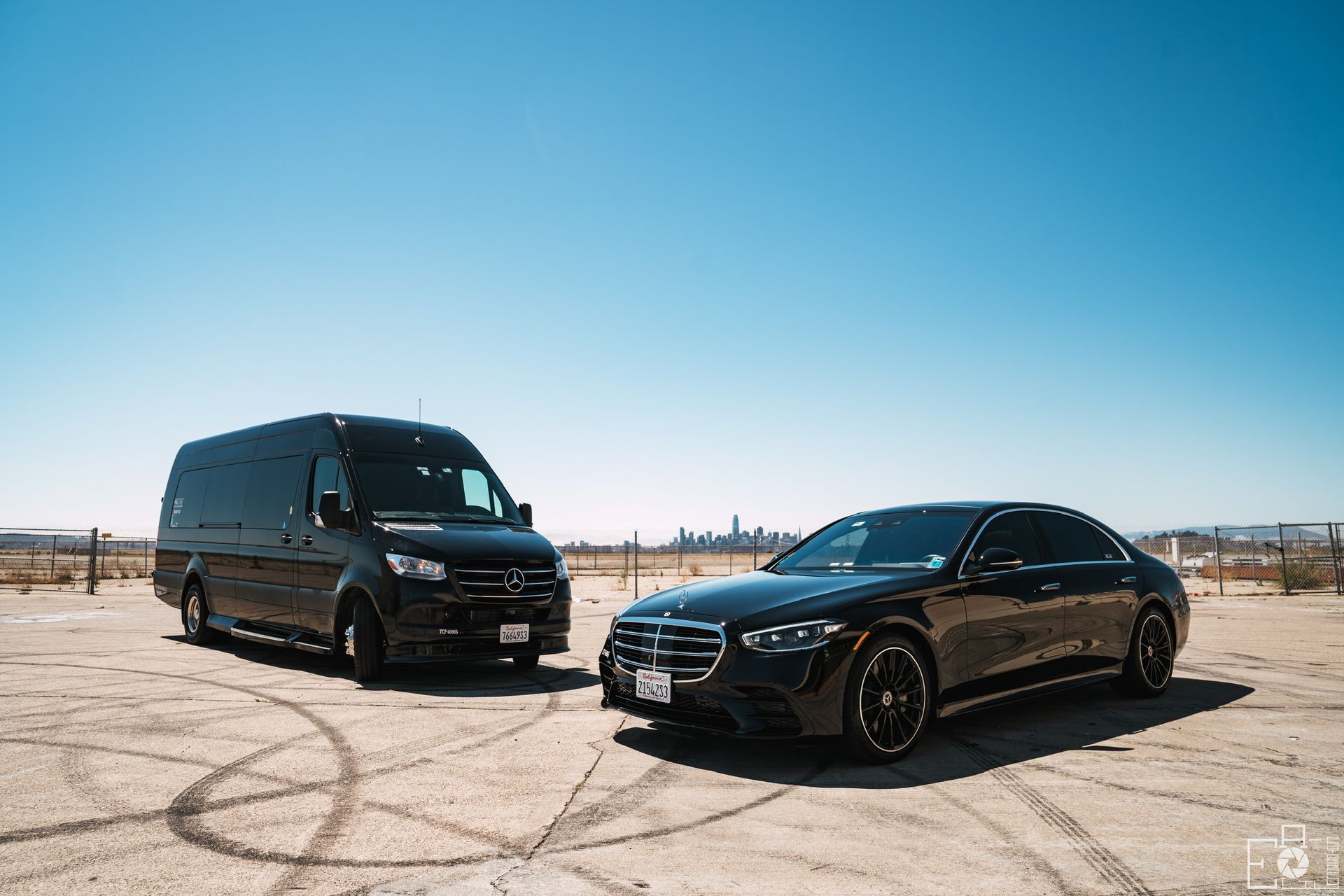 A van and a car are parked next to each other in a dirt field.