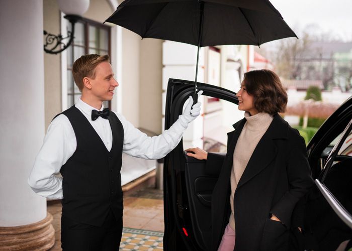 A man is opening the door of a car for a woman holding an umbrella.