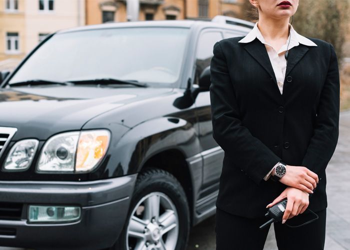 A woman in a suit is standing in front of a black suv.