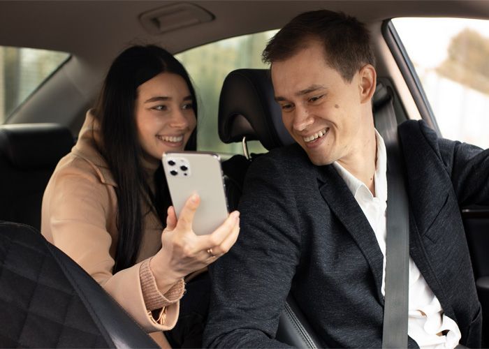 A man and a woman are sitting in a car looking at a cell phone.