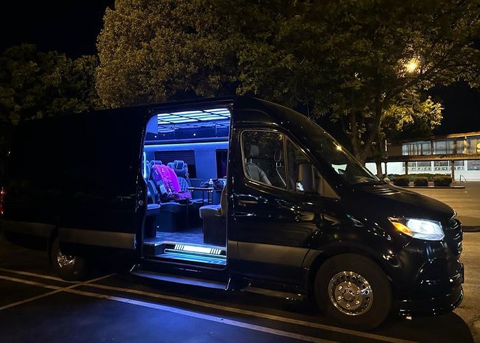 A black van is parked in a parking lot at night with the door open.