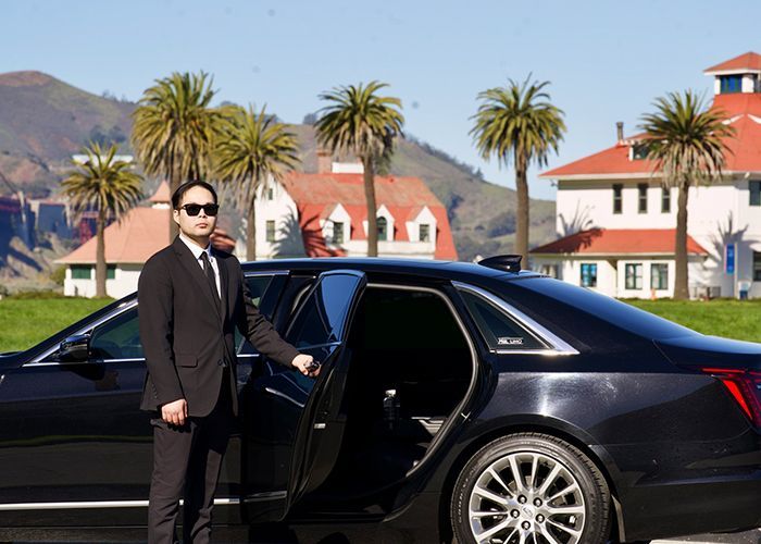 A man in a suit and tie is standing next to a black car.
