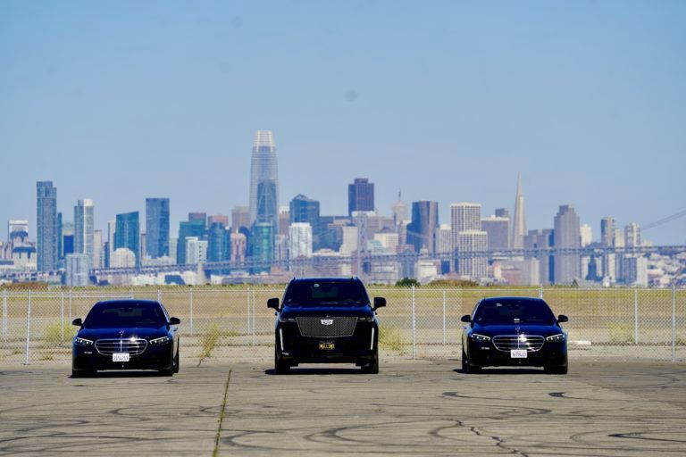Three cars are parked in a parking lot in front of a city skyline.