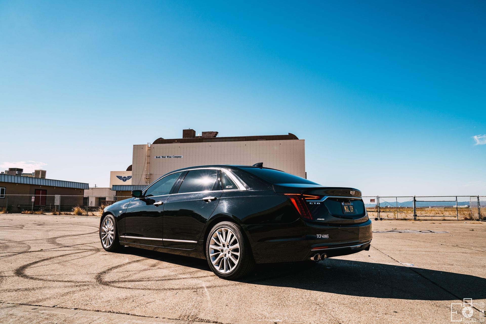 A black car is parked in a parking lot in front of a building.
