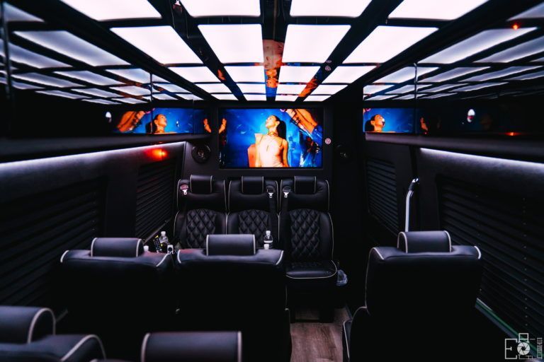 Inside a luxury vehicle: black leather seating, multiple screens playing video, and ambient lighting.