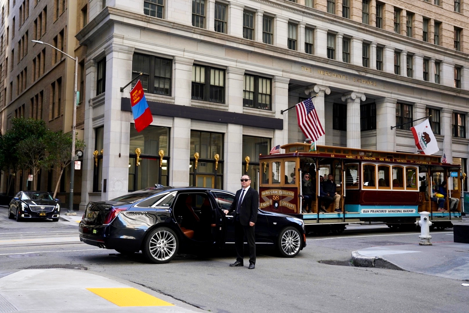 Black car and man in a suit beside a cable car in San Francisco outside a grand building