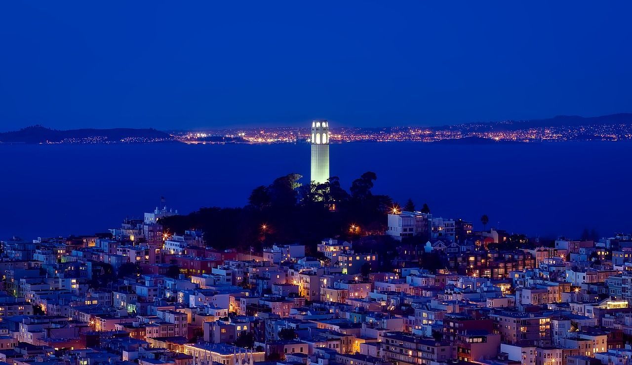 An aerial view of a city at night with a lighthouse in the distance